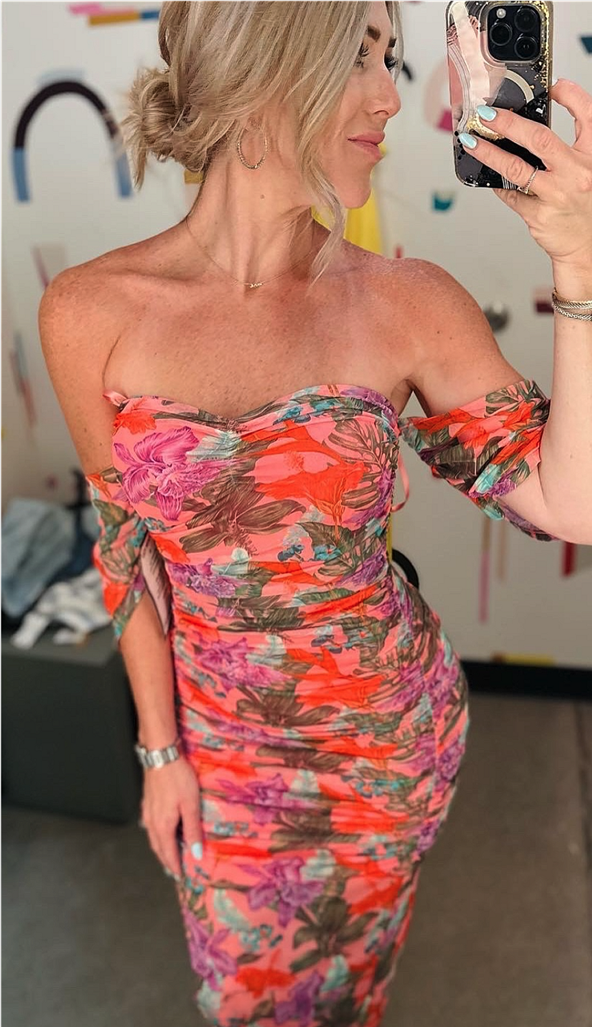 Woman in floral dress taking mirror selfie.